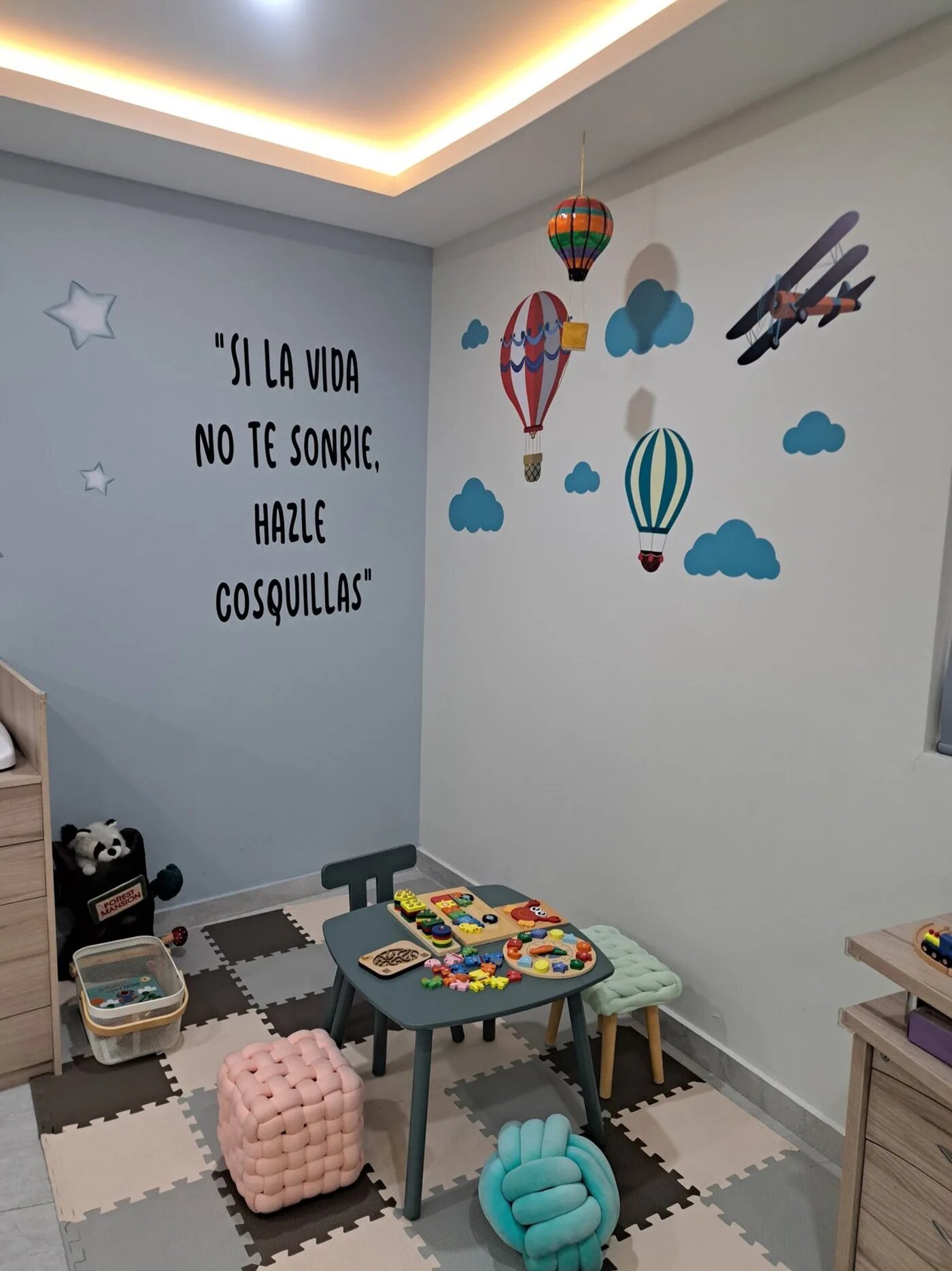 Rincón de juegos con mesa infantil, juguetes didácticos y globos aerostáticos en la pared